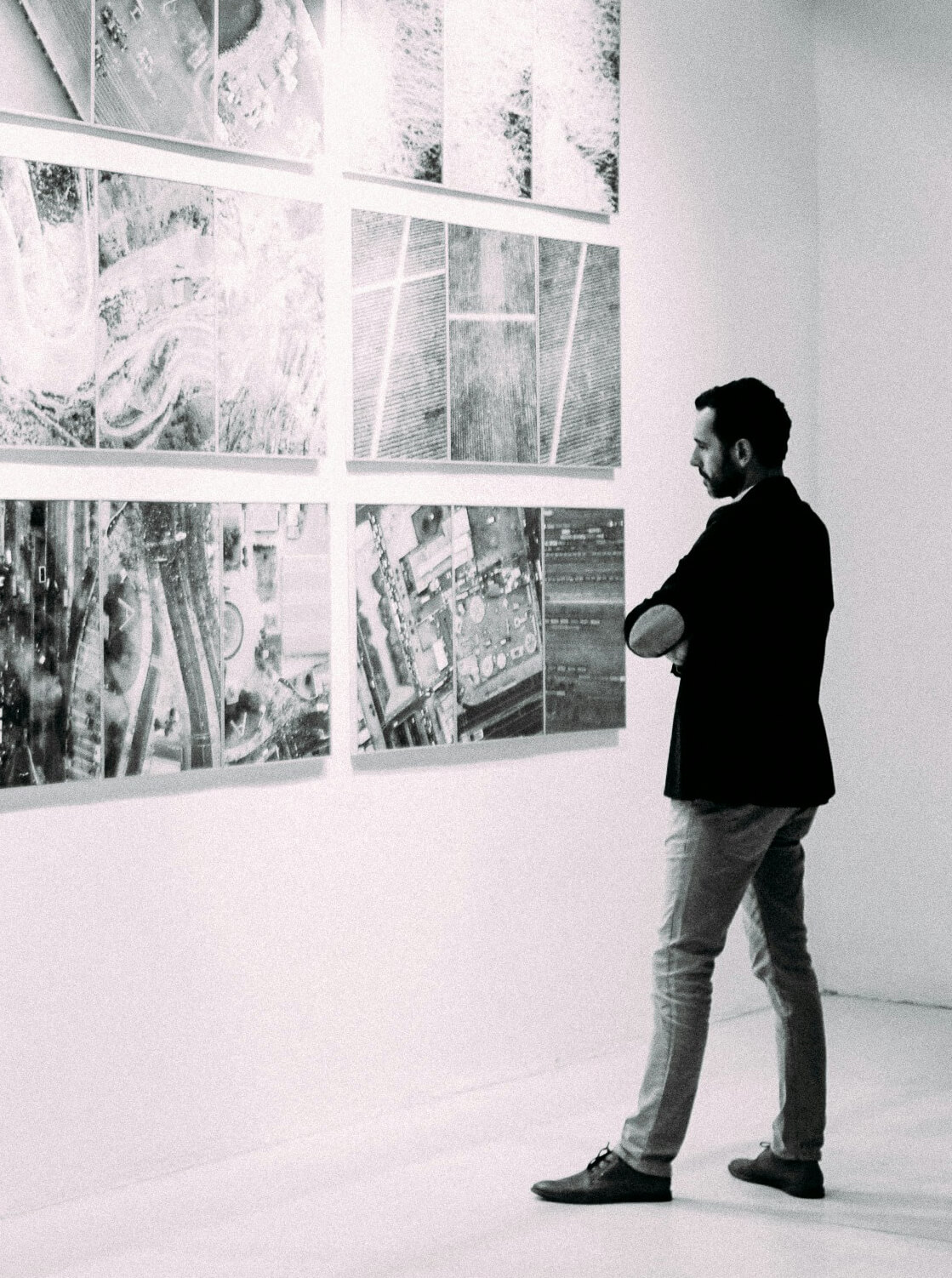 Man in a blazer thoughtfully observing a wall display of black-and-white abstract photographs in a gallery.