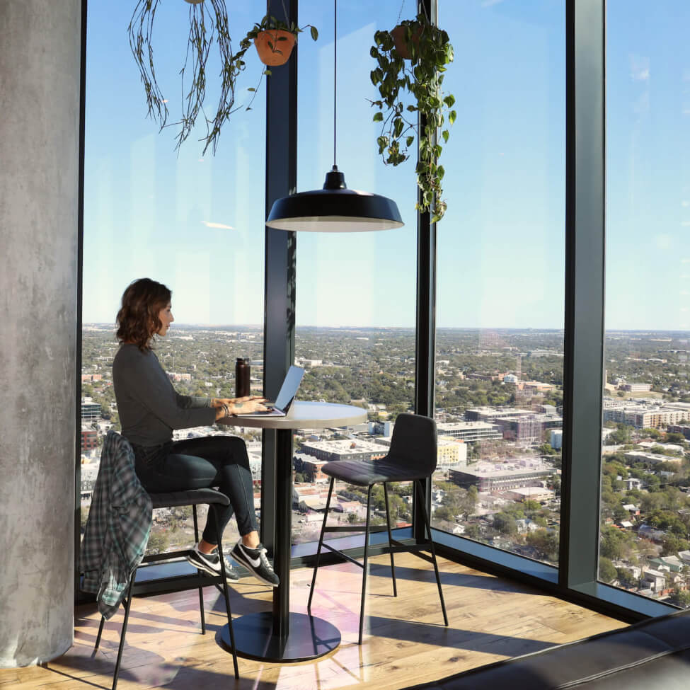 Interior image of woman working on her computer in the rooftop club house of The Vesper Residences in Downtown Austin with awesome floor to ceiling skyline views.