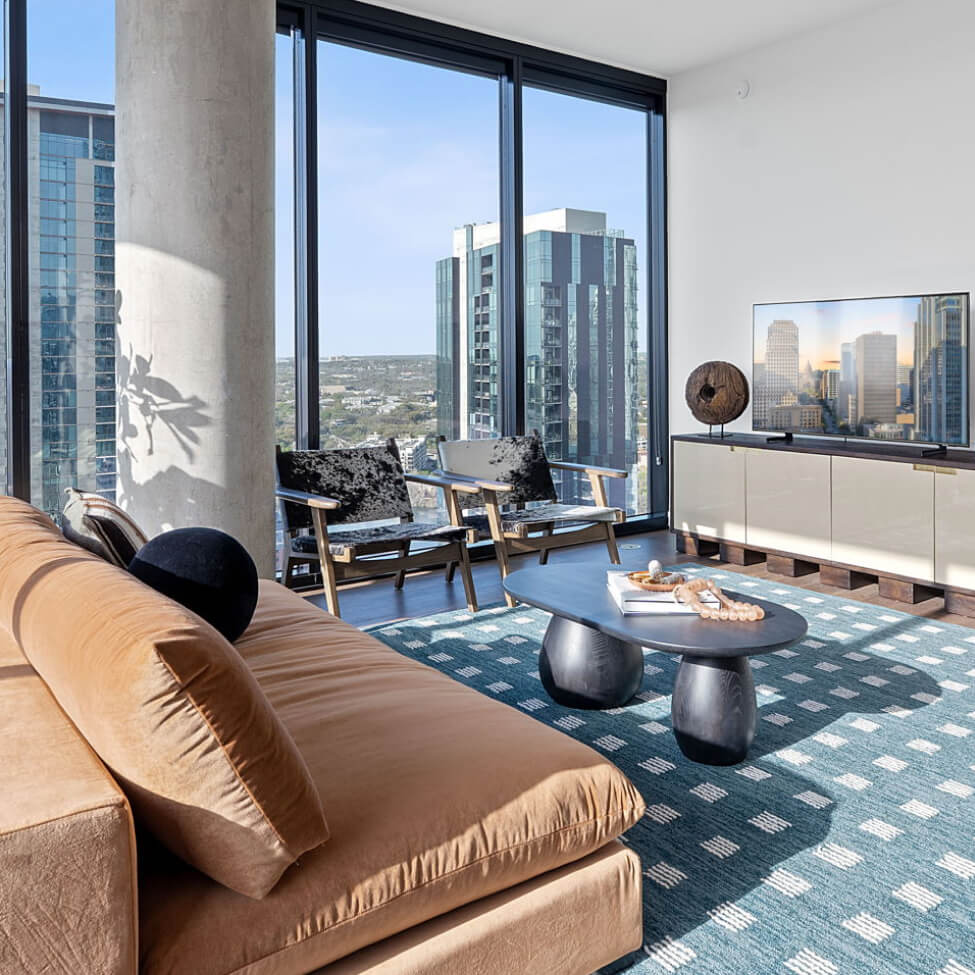 Living room at Vesper Residences with floor-to-ceiling windows, a tan sofa, and downtown Austin views.